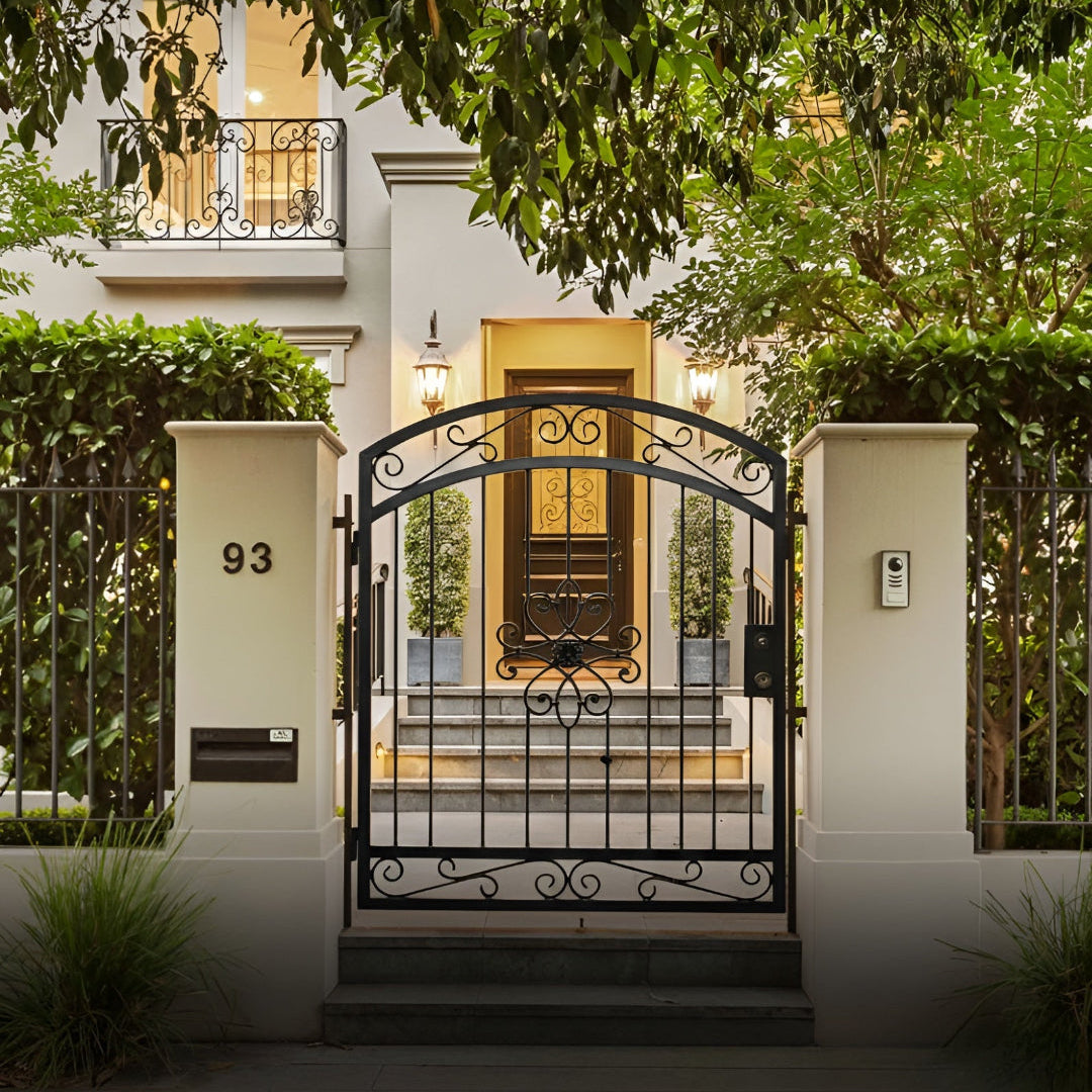 Decorative garden entrance gate set between stone pillars beside a traditional stone house; a black metal gate with intricate geometric starburst cutouts