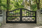Black metal gates leading to a driveway with trees and a house in the background