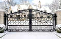 Decorative black metal gate in front of a house with snow on the ground