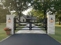 Wooden gate with stone pillars on a driveway leading to a house.