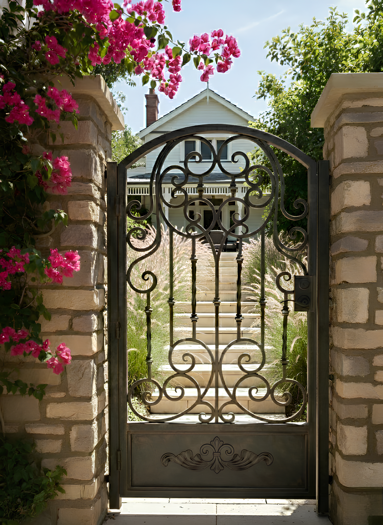 Decorative wrought iron gate with pink flowers and a house in the background